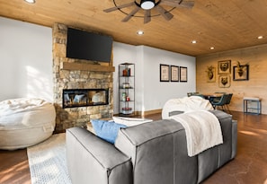 A living room with a stone fireplace, a grey sofa, a bookshelf, and framed pictures on the wall. - Sweet Dreams: Cozy Elegance • Hot-Tub • FireTable • Arcade Game • Mtn Views • EV (Blue Ridge)