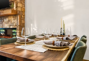 A dining table set with plates, glasses, and napkins, with a stone wall and fireplace in the background. - Sweet Dreams: Cozy Elegance • Hot-Tub • FireTable • Arcade Game • Mtn Views • EV (Blue Ridge)