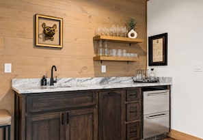 A kitchen with wooden cabinets, a marble countertop, a stainless steel refrigerator, and a shelf with glasses and a vase. - Sweet Dreams: Cozy Elegance • Hot-Tub • FireTable • Arcade Game • Mtn Views • EV (Blue Ridge)