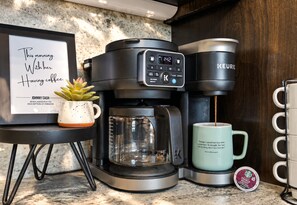 A coffee maker, a mug, a framed quote, and a small potted plant on a kitchen counter.