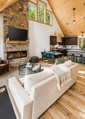 A spacious living room with a stone fireplace, a large sofa, and a dining area with blue chairs.
