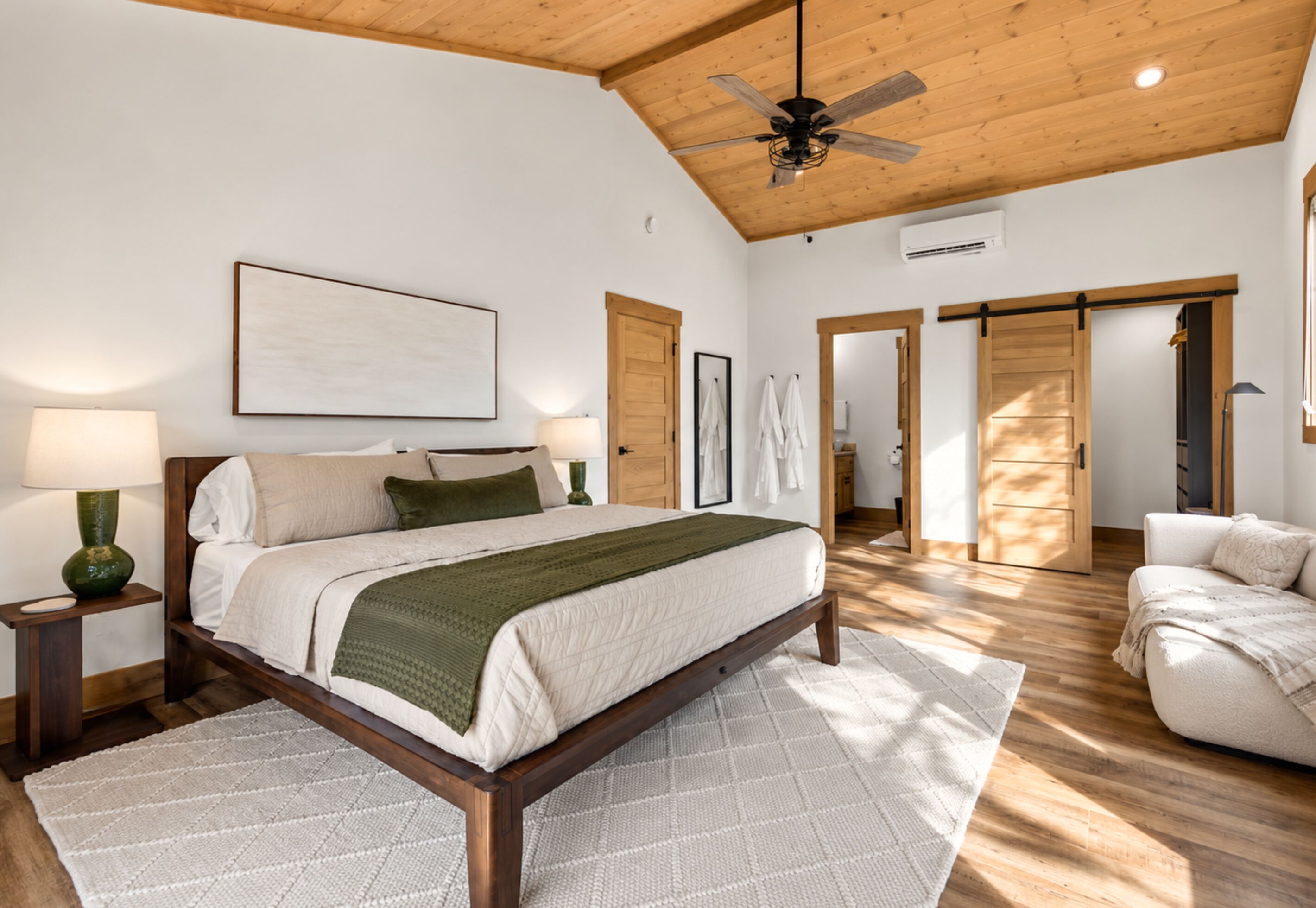 A bedroom with a bed, bedside tables, a ceiling fan, a large window, and a sliding door leading to another room.