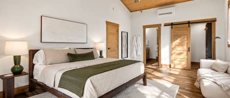 Ein Schlafzimmer mit Bett, Nachttischen, Deckenventilator, großem Fenster und einer Schiebetür zu einem anderen Raum.