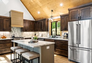 A kitchen with wooden cabinets, a stainless steel refrigerator, and a marble countertop.