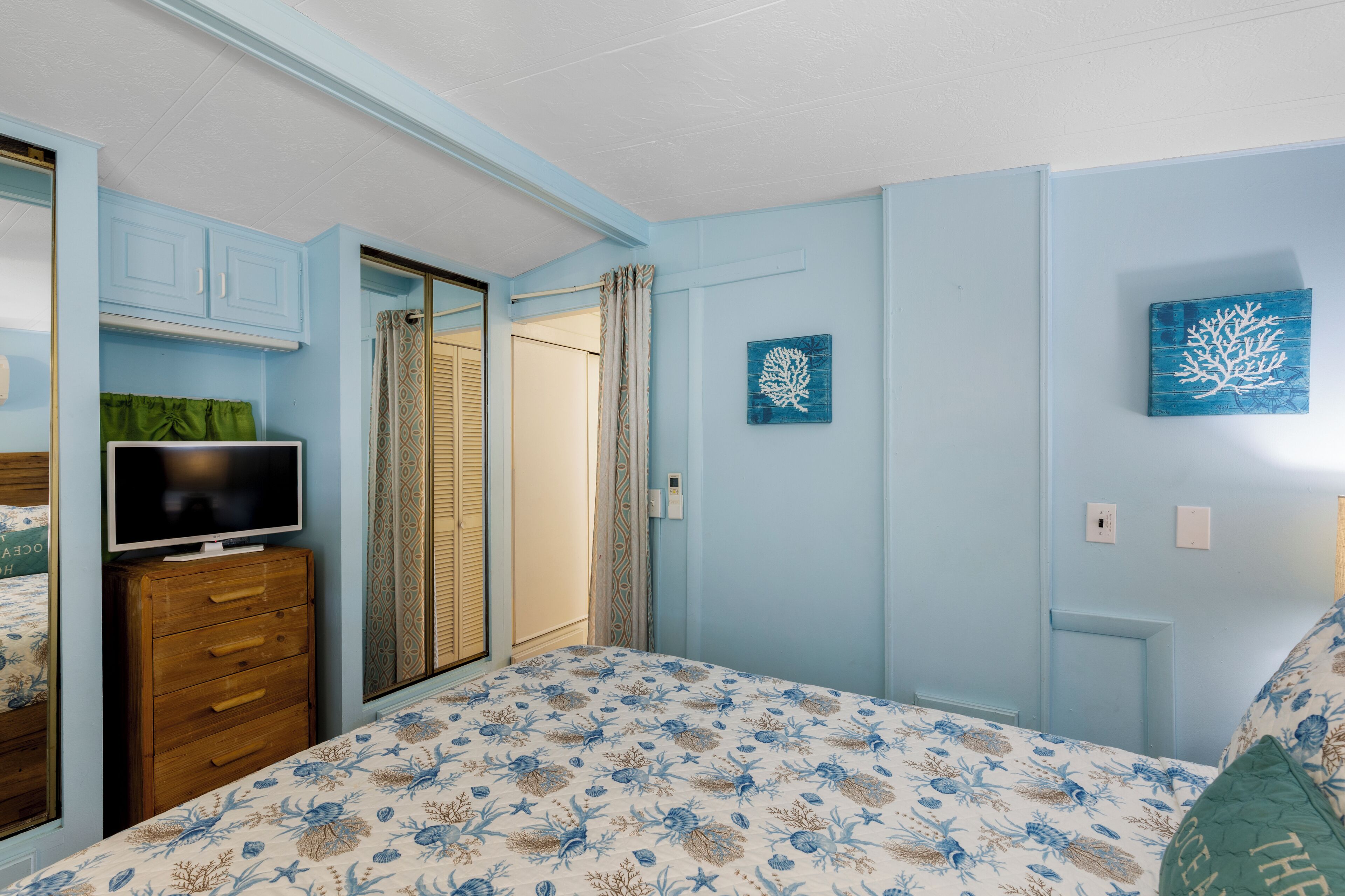 Une chambre à coucher avec un lit, un téléviseur posé sur une commode et deux œuvres d’art accrochées au mur.