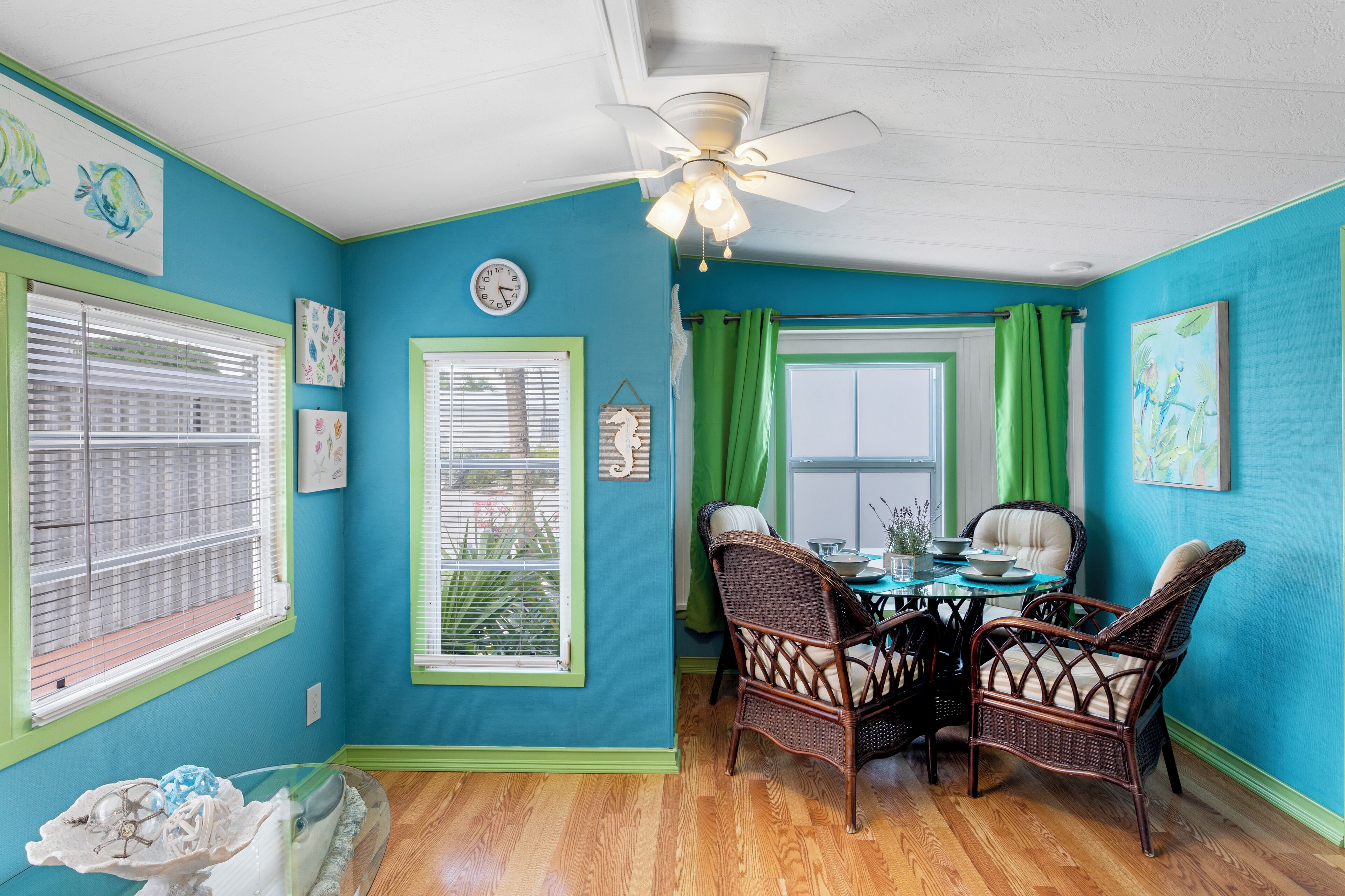 A dining area with a round table, wicker chairs, and a ceiling fan.