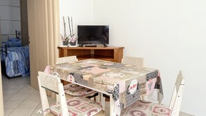 A dining area with a table covered in a patchwork tablecloth, surrounded by chairs with patterned cushions. A television is mounted on a wooden stand against the wall. - P062 - Porto Recanati, two-room apartment in the center 30 meters from the sea (Porto Recanati)