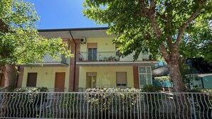Ein zweistöckiges Gebäude mit Balkon, geschlossenem Zaun und Bäumen im Vordergrund.