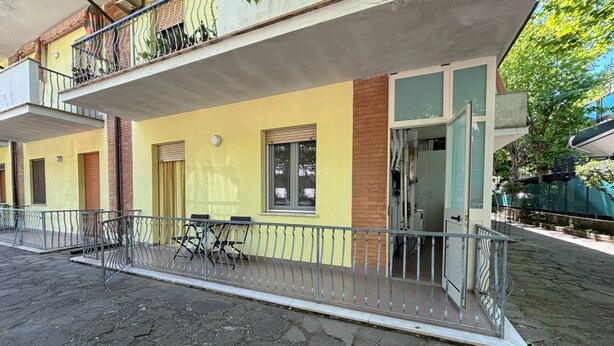 Ein Gebäude mit gelber Fassade, einem Balkon mit Metallgeländern und einem gepflasterten Eingangsbereich.