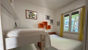 Ein Schlafzimmer mit Etagenbetten, einem Fenster mit gelben Vorhängen und einer kleinen, orangefarbenen Regaleinheit.