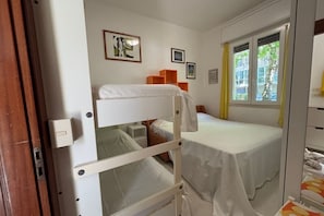 A room with bunk beds, a window with curtains, and a small desk with a chair. - CN012 – Cesenatico, One-Bedroom Apartment with Air Conditioning and Parking (Cesenatico)