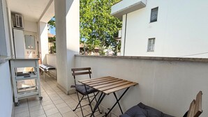 Un pequeño patio exterior con una mesa plegable y dos sillas, un carrito metálico y una pared blanca.