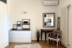Une pièce avec une commode blanche, un miroir, une chaise en bois, un radiateur et une plante en pot.