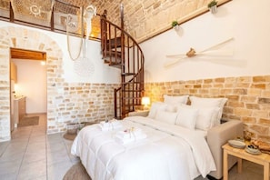 A bedroom with a stone wall, a wooden spiral staircase, a bed with white bedding, and a small table with plates and olives. - Elisa - Inside a 500 years old tower (Giovinazzo)