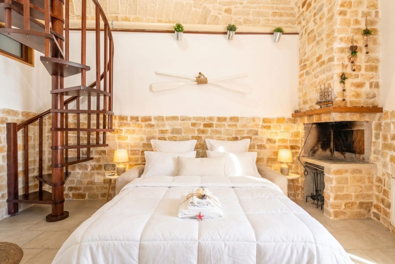 Une chambre avec un escalier en colimaçon en bois, un mur en pierre, une cheminée et un lit avec une literie blanche.