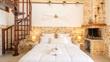 Un dormitorio con una escalera espiral de madera, pared de piedra, chimenea y cama con ropa de cama blanca.