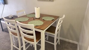Un tavolo da pranzo con quattro sedie bianche, un vaso al centro e un quadro incorniciato sopra.