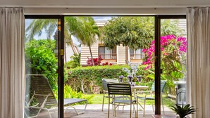 A room with a sliding glass door leading to an outdoor patio with a table, chairs, and a potted plant. - Cozy ground floor condo, lush lanai, dining nearby (Kihei)