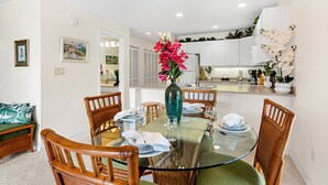 A dining area with a glass table, wooden chairs, and a vase with flowers. - Cozy ground floor condo, lush lanai, dining nearby (Kihei)