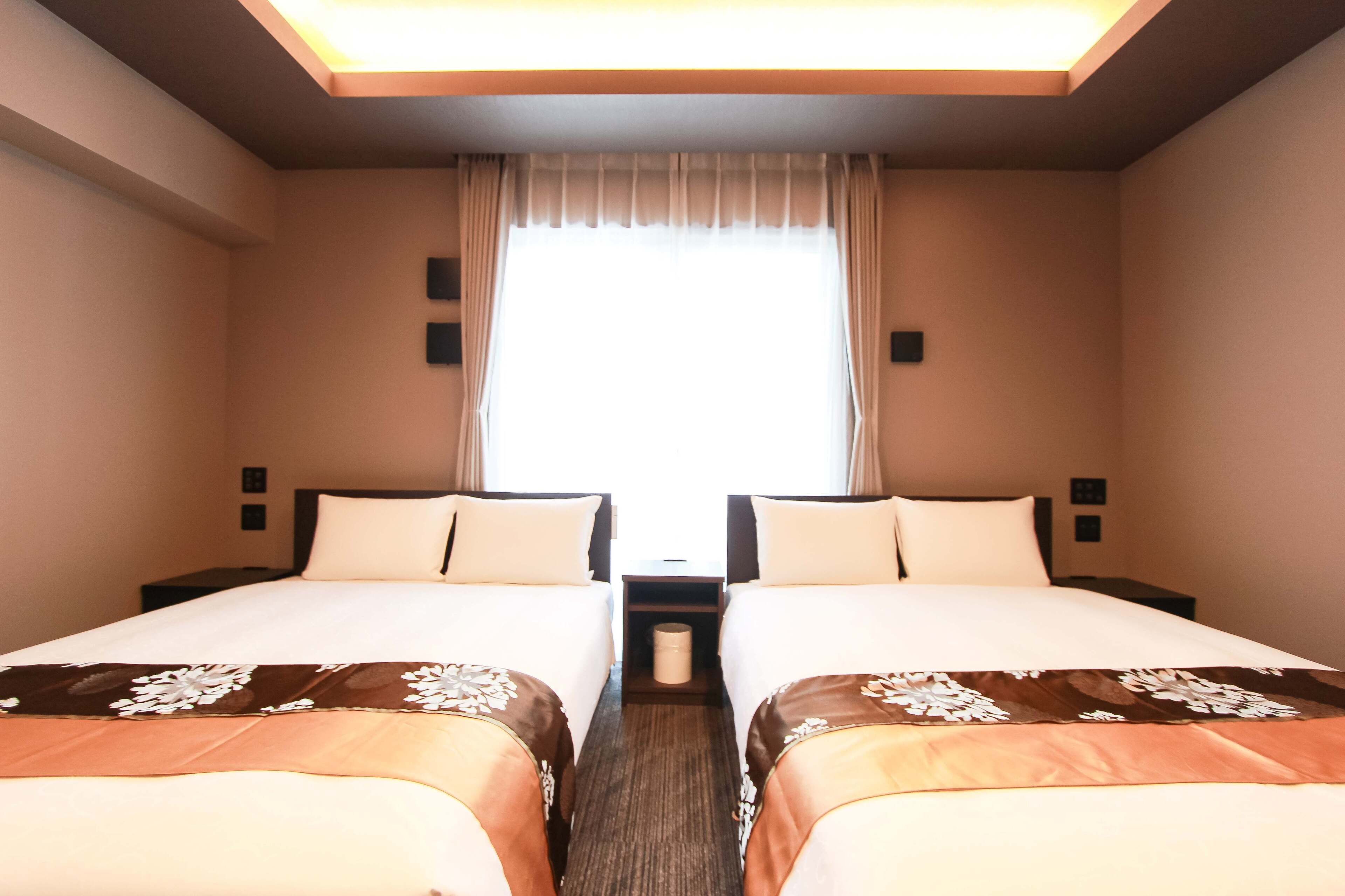 Habitación de hotel con dos camas, un ventanal con cortinas, una mesita y lámparas de pared.