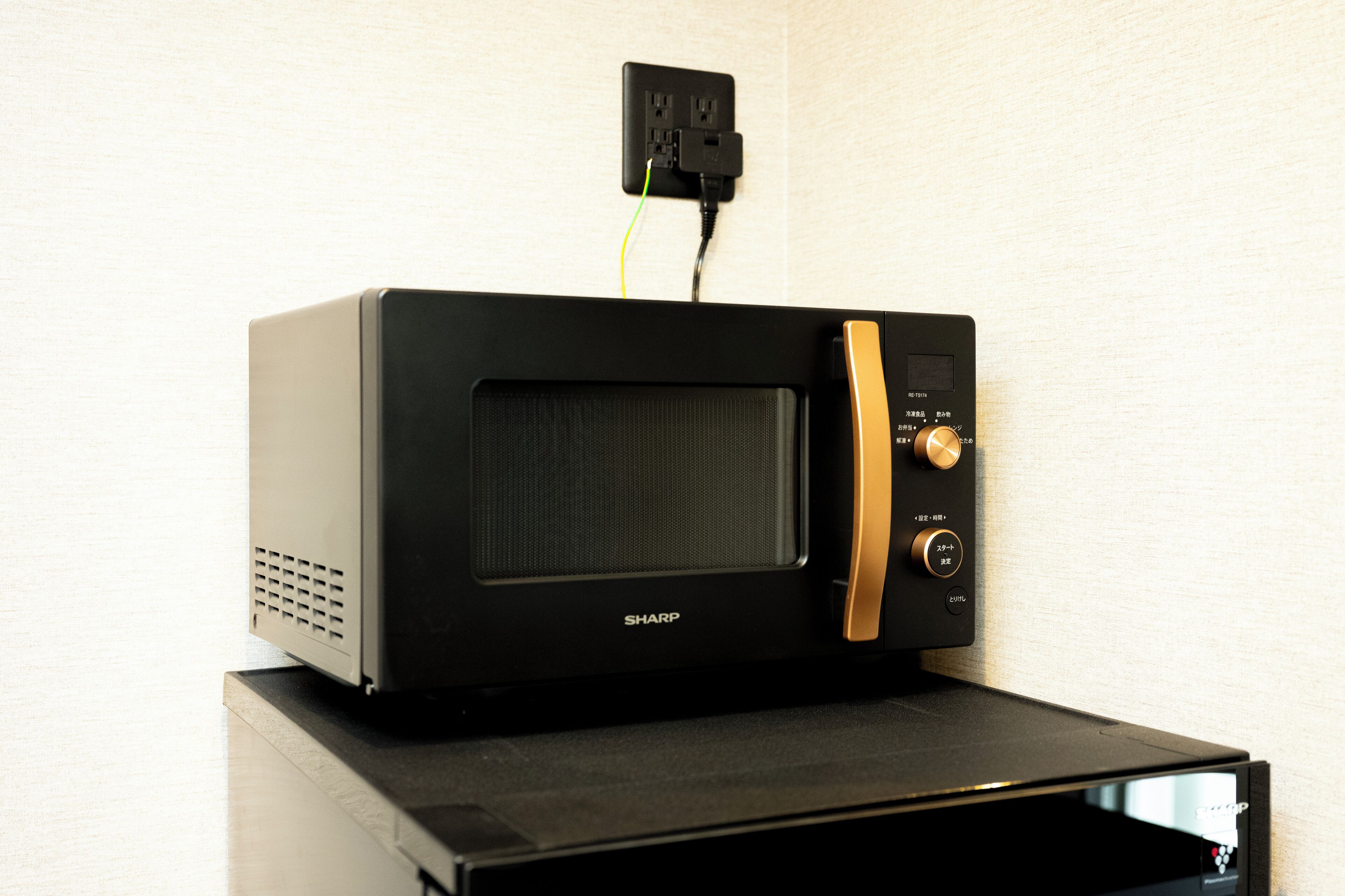 A black Sharp microwave oven with a gold control panel, plugged into a wall socket.