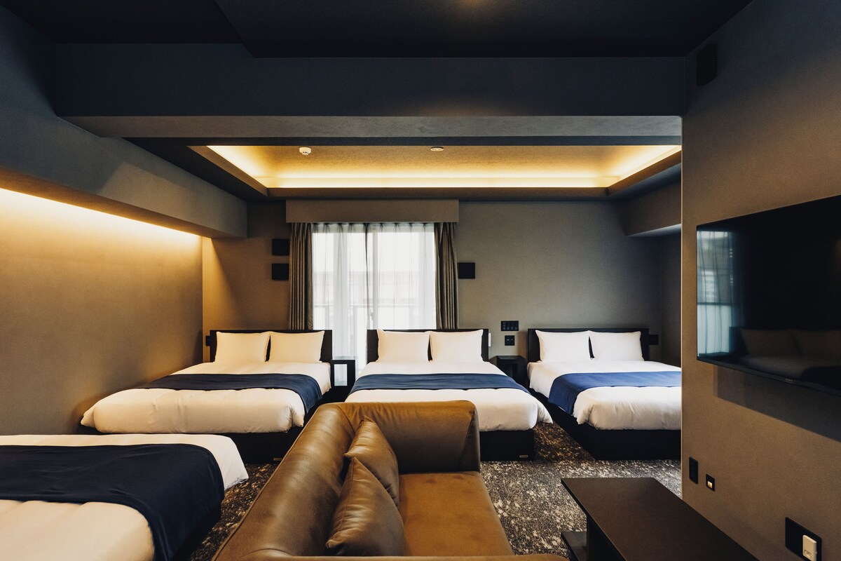 Een hotelkamer met drie bedden, een slaapbank, een flatscreen-tv en een groot raam met gordijnen.