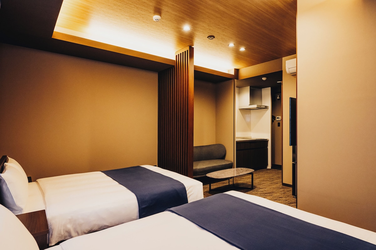 Een hotelkamer met twee bedden, een bank, een kleine tafel en een kitchenette.