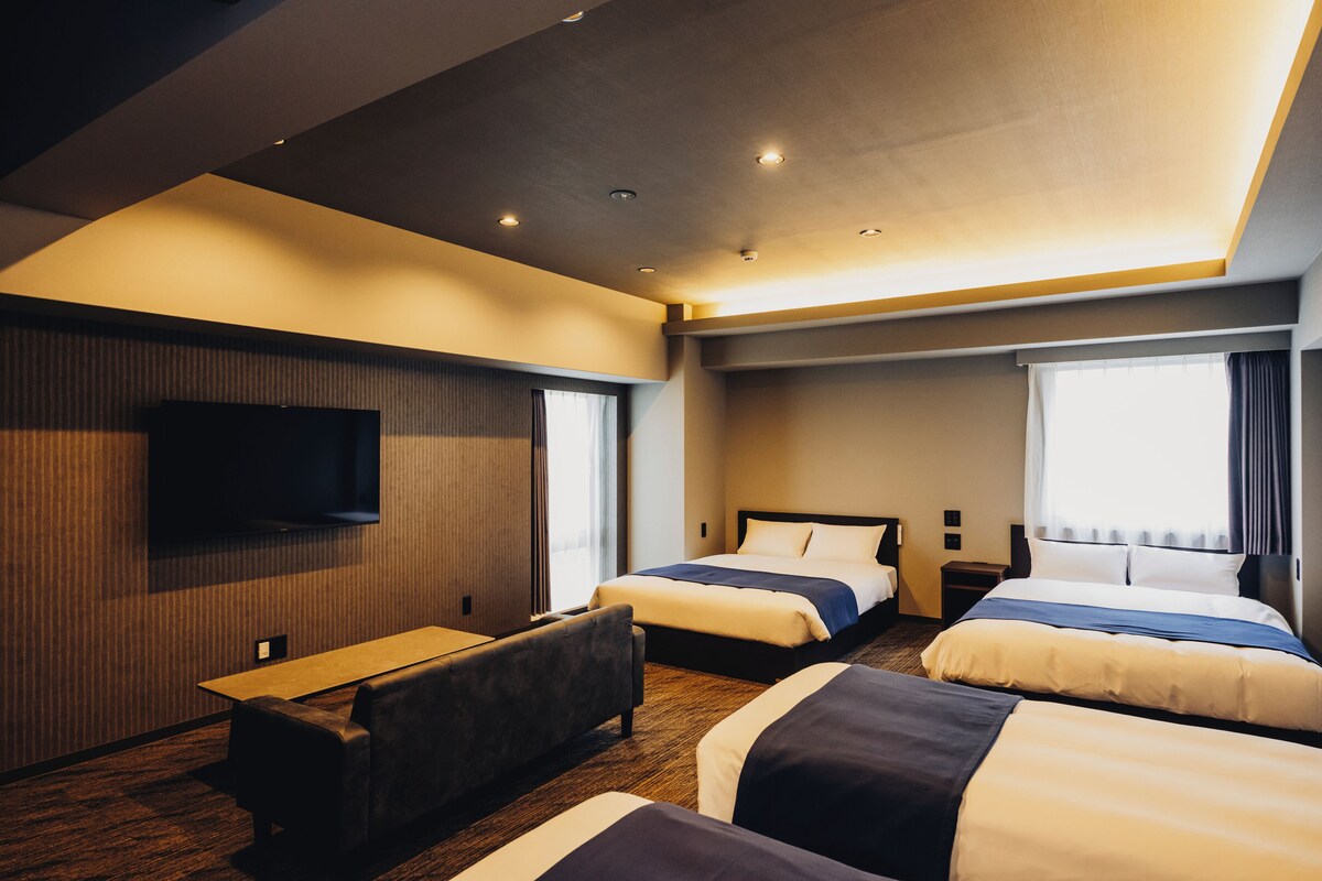Een hotelkamer met twee bedden, een flatscreen televisie aan de muur, een bureau en een raam met gordijnen.