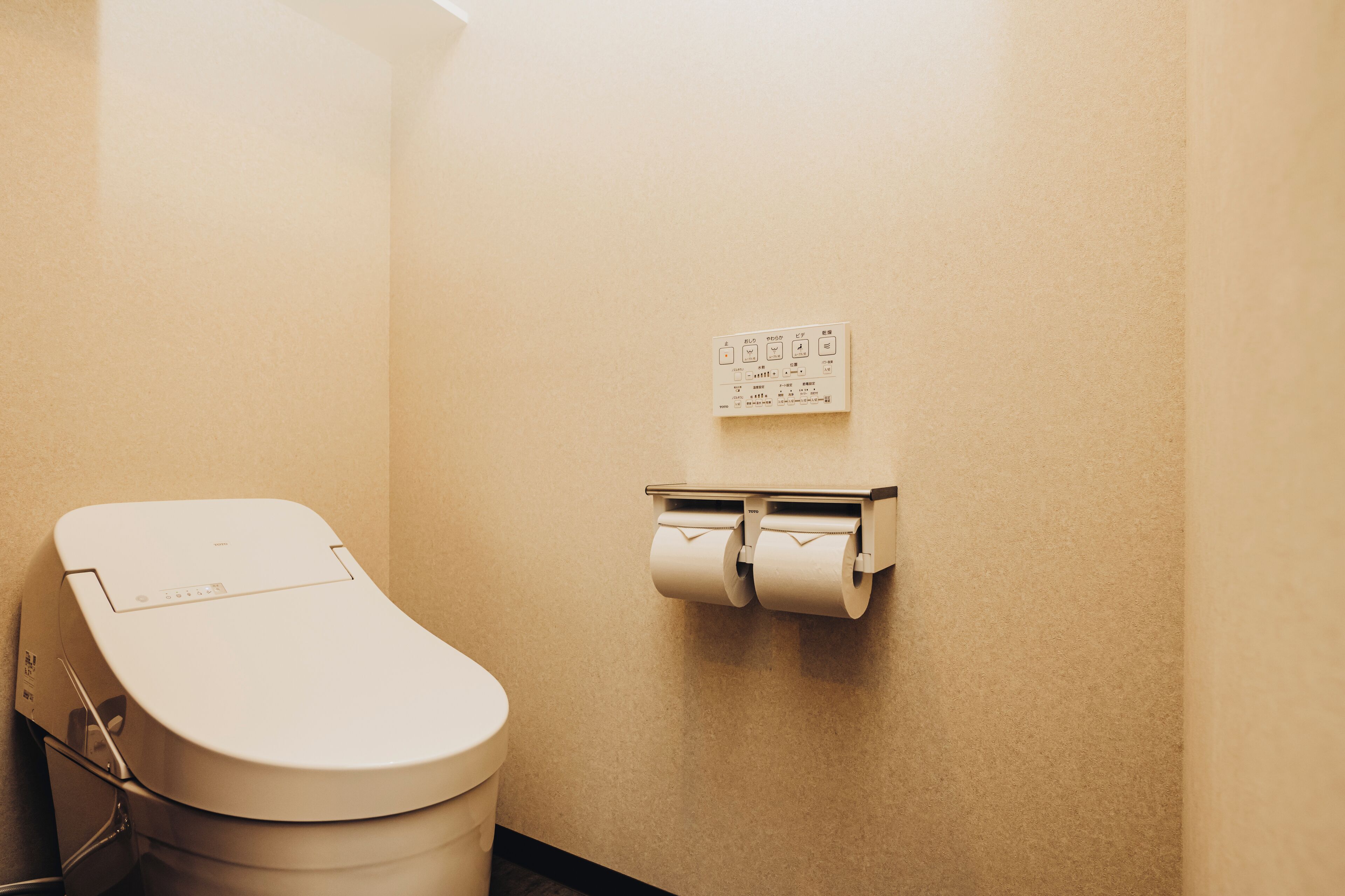 A toilet with a paper towel dispenser and a flush button on the wall.