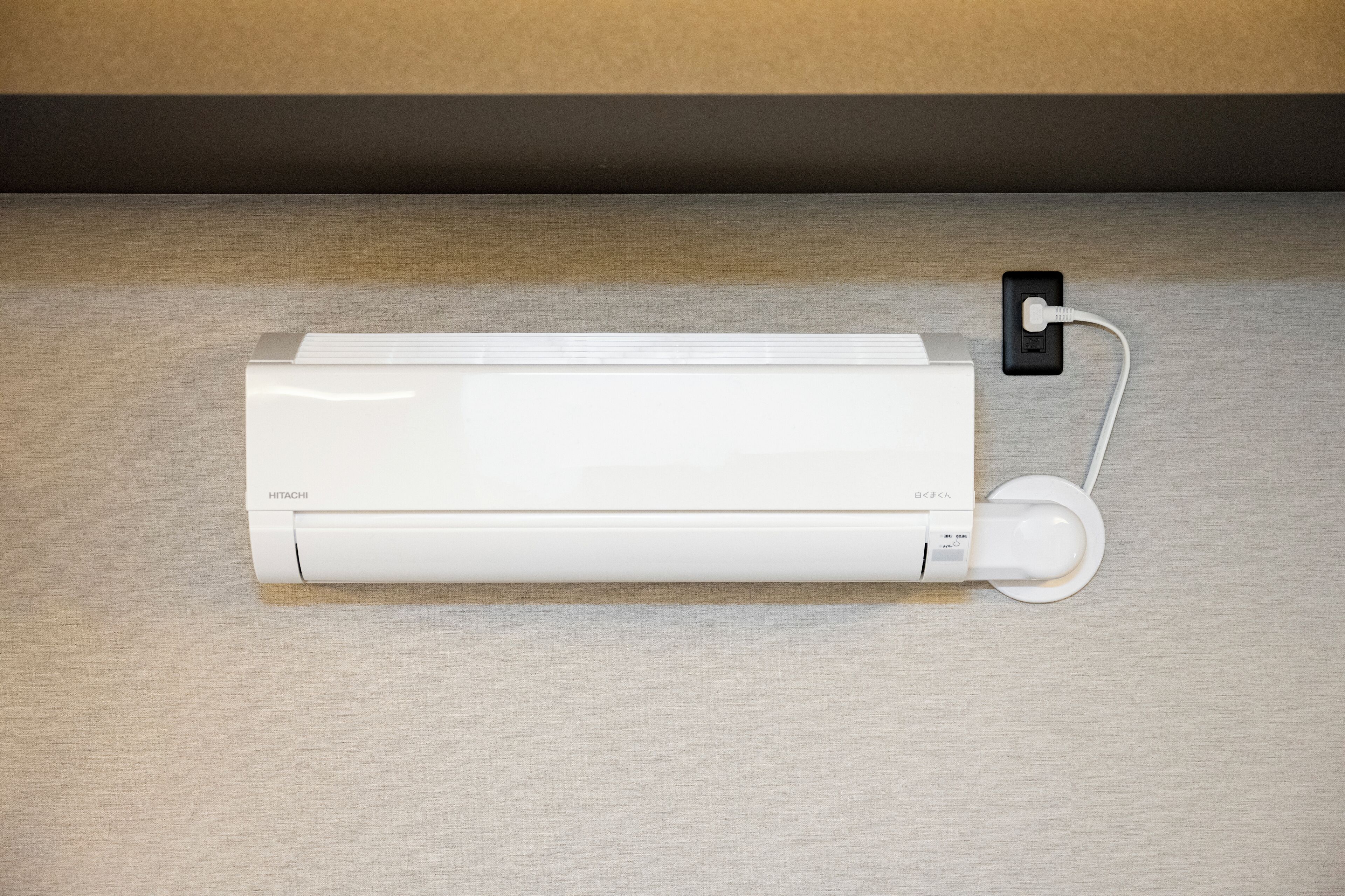 A white air conditioning unit with a control panel and a power cord plugged into a wall socket.