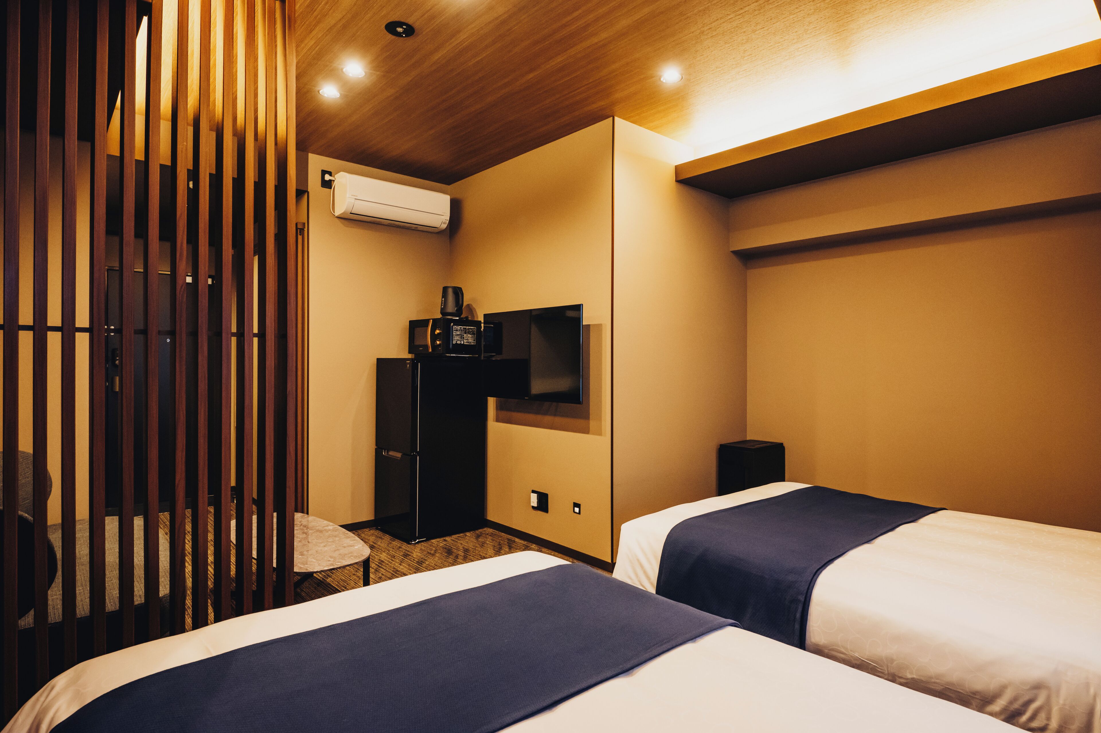 A hotel room with two beds, a TV, a microwave, and an air conditioning unit.