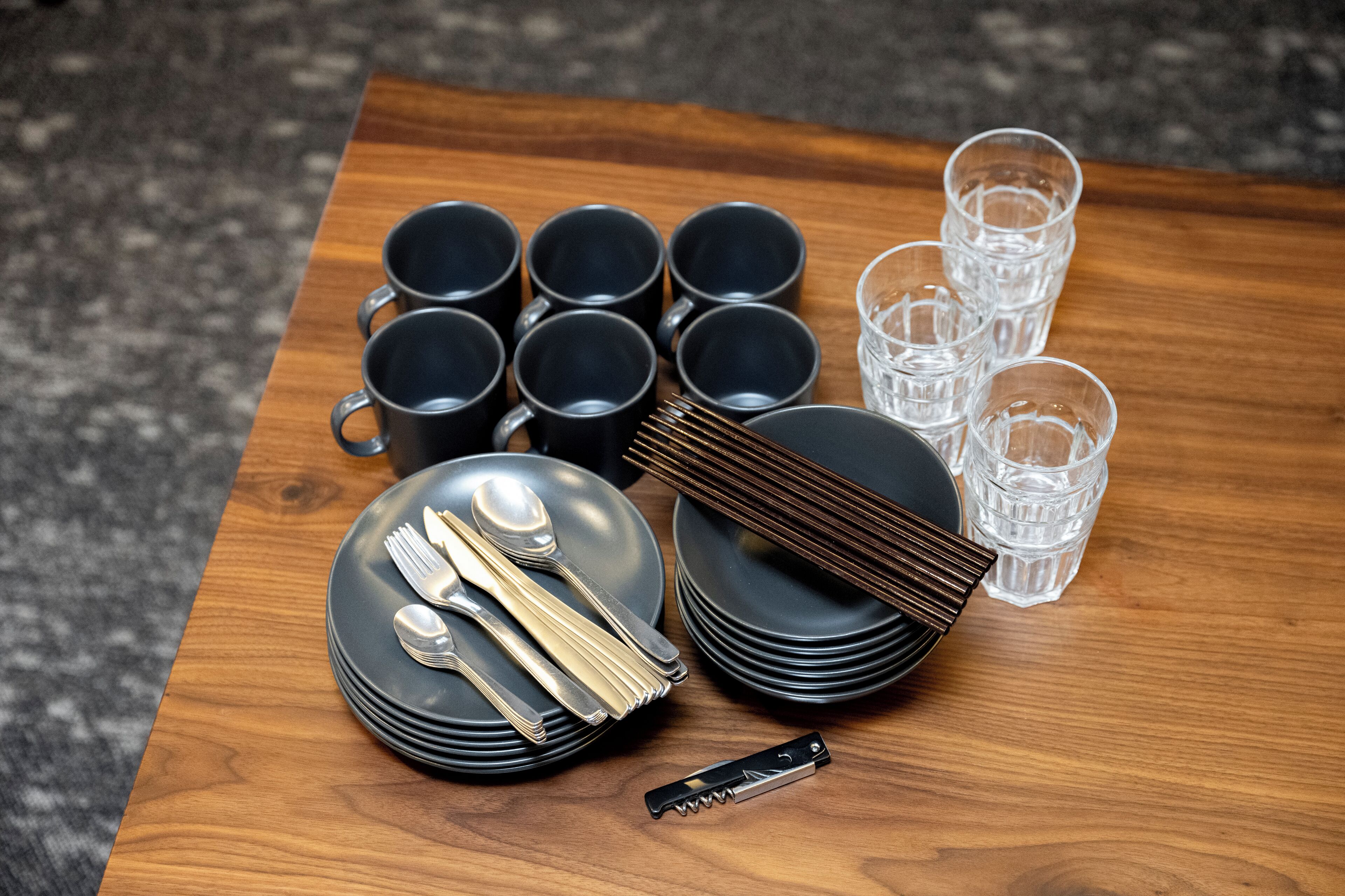 A neatly arranged table with black plates, silverware, and clear glasses on a wooden surface.