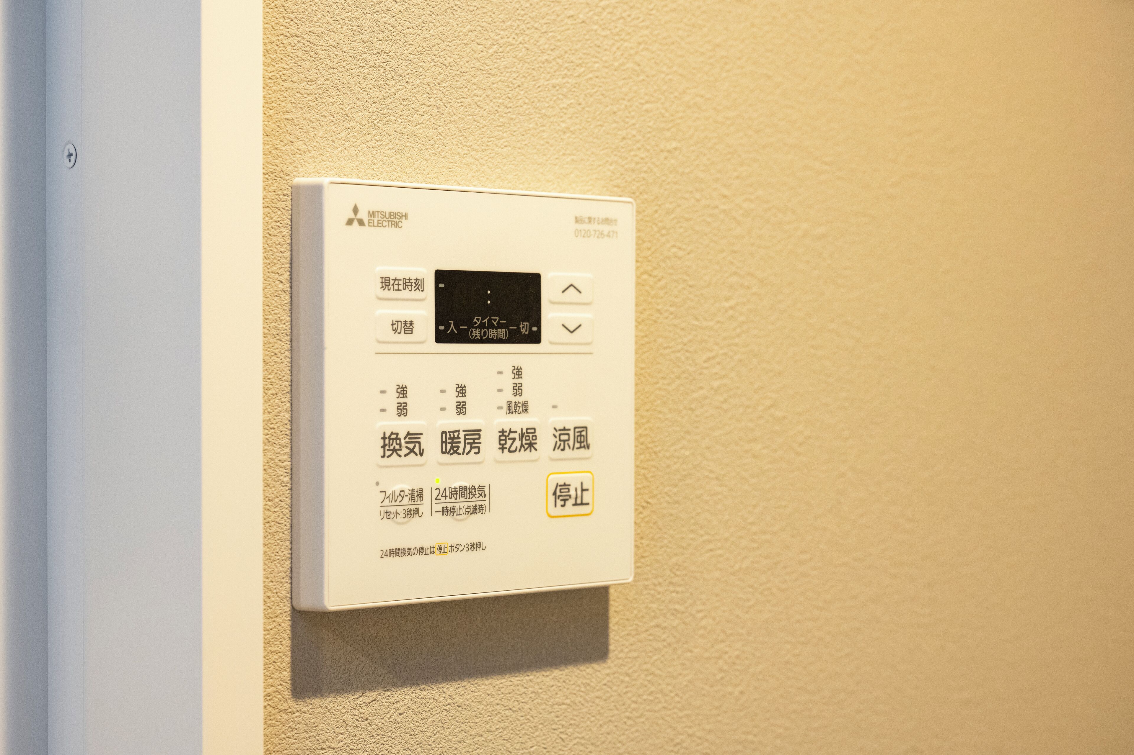 A Mitsubishi Electric thermostat mounted on a beige textured wall.