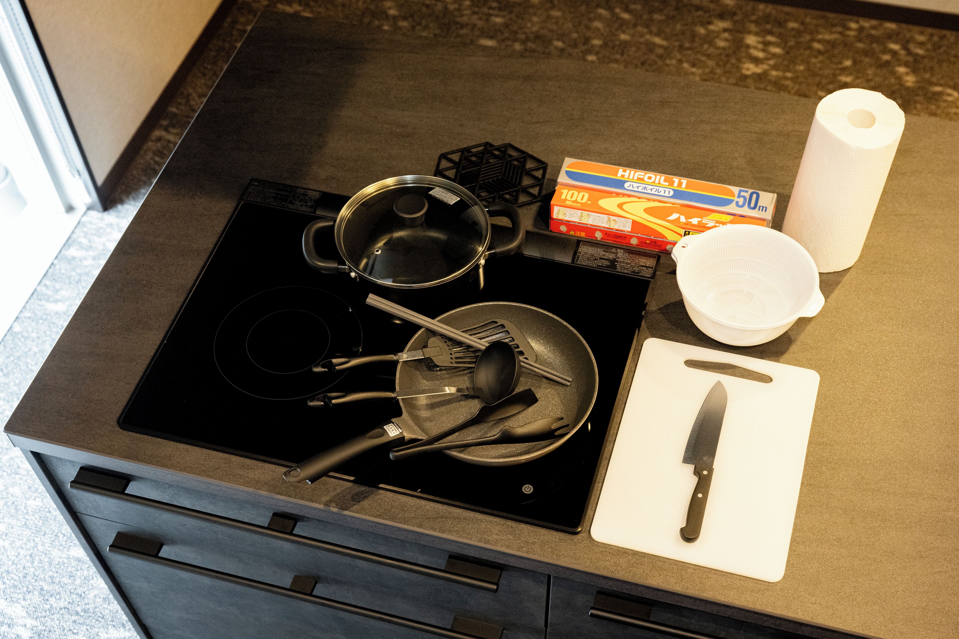 Eine Küche mit Herd, Töpfen, einer Pfanne, einer Packung Küchenpapier und einem Schneidebrett mit Messer.