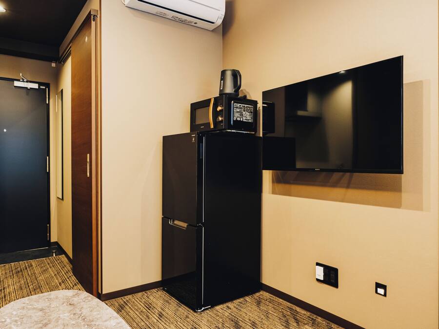A hotel room with a black refrigerator, a flat-screen TV mounted on the wall, a carpeted floor, and a door with a handle.