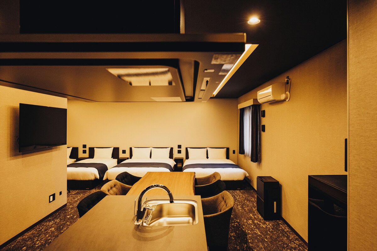 Een hotelkamer met twee bedden, een aan de muur bevestigde televisie, een wastafel en een klein tafeltje.