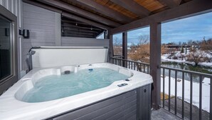 A hot tub on a covered deck with a view of a snowy landscape.