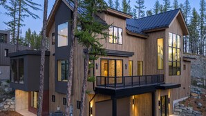 A modern two-story house with a wooden exterior, large windows, and a balcony.