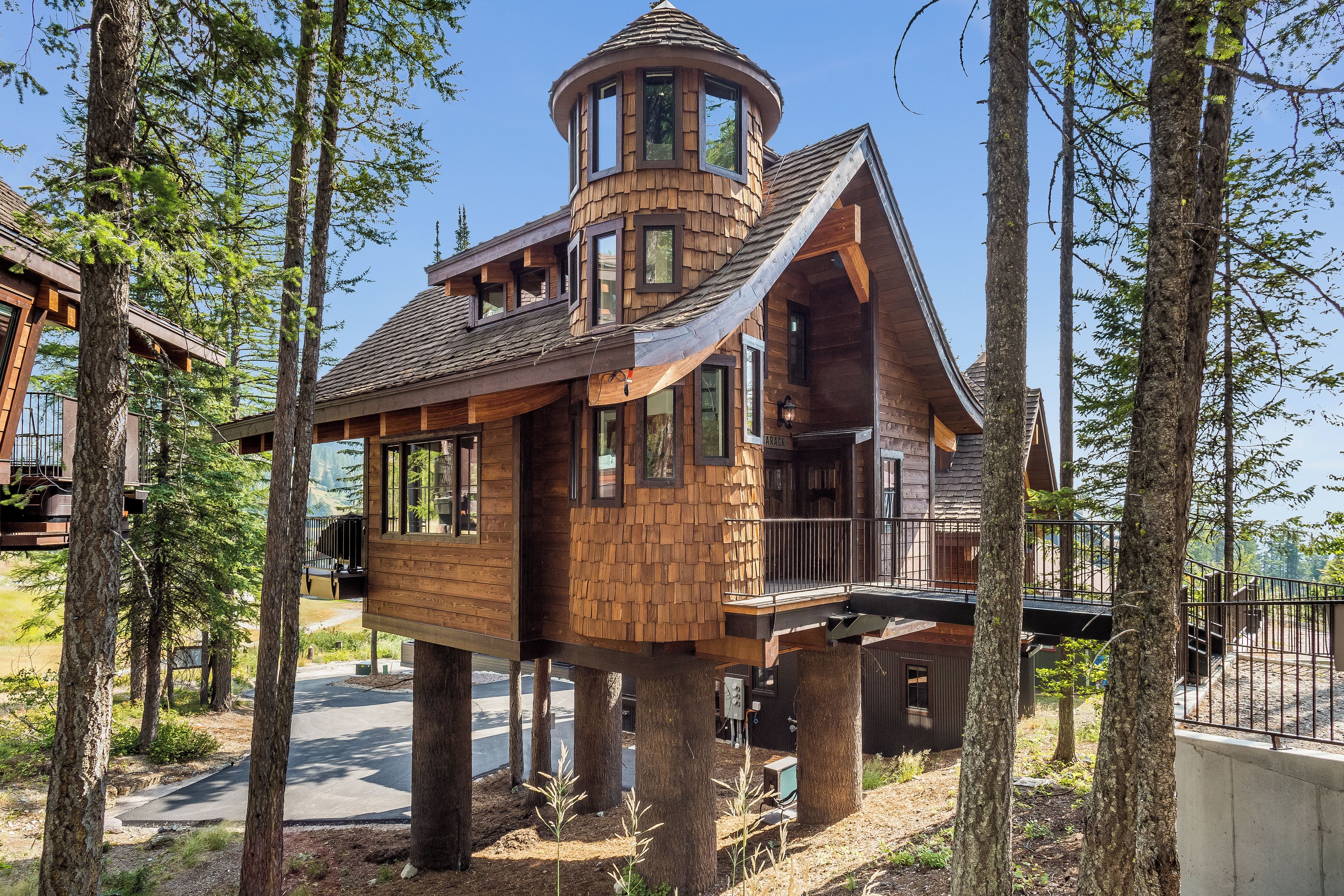 Une cabane en bois dotée d’une tour circulaire, de grandes fenêtres et d’un balcon.