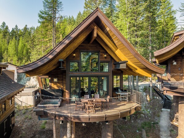 A wooden cabin with a deck and large windows, surrounded by trees.