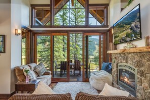 A spacious living area with a fireplace, a large window offering a view of a forest, and a cozy seating arrangement.