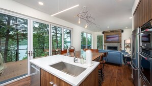 A modern kitchen with a large island, wooden cabinets, and a view of a lake. - NEW private hot tub & amazing lake views (Whitefish)