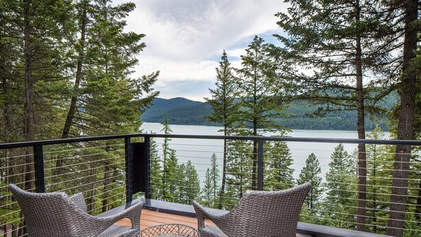 A balcony with wicker chairs and a small table, overlooking a lake and forested mountains. - NEW private hot tub & amazing lake views (Whitefish)