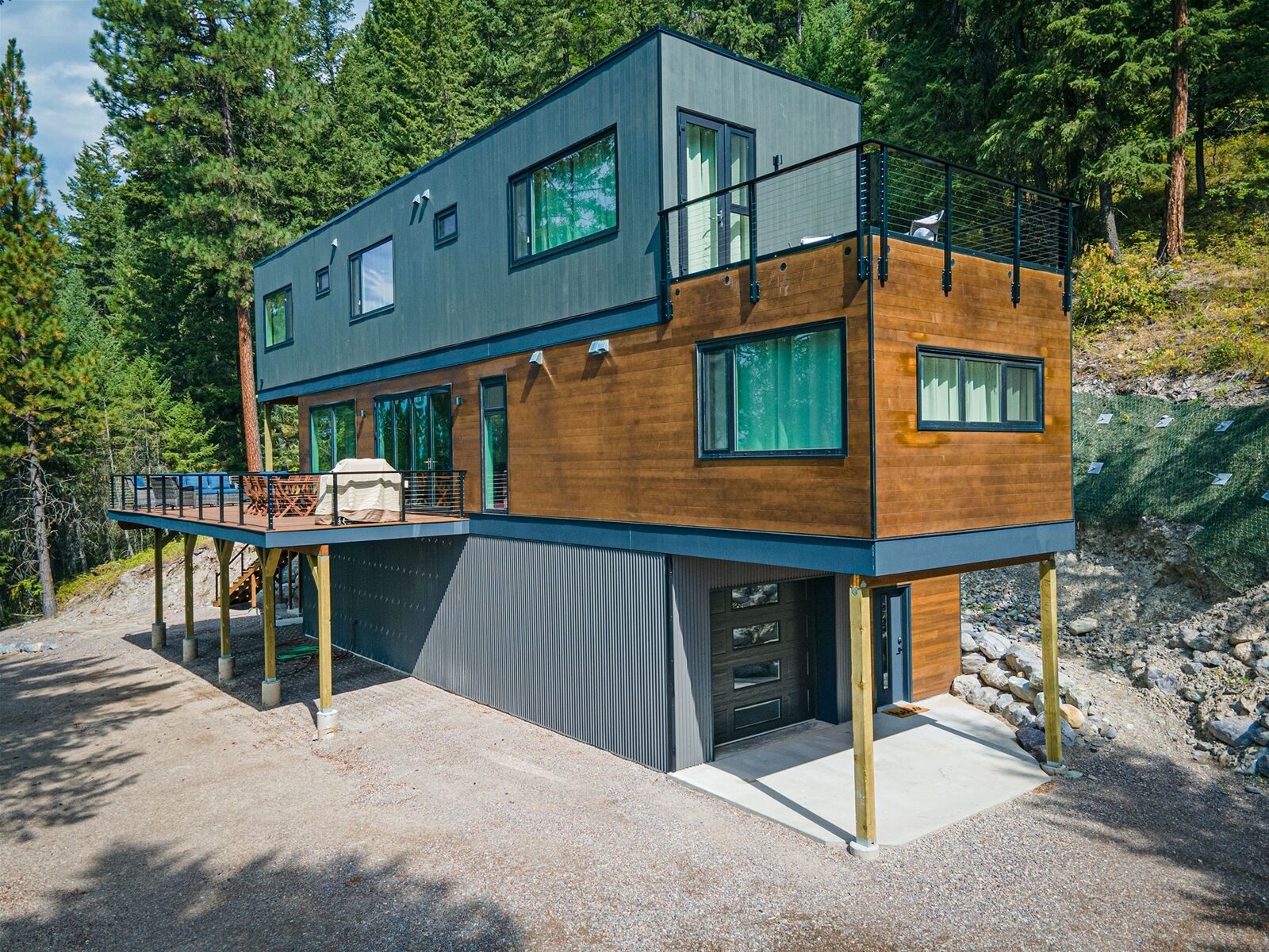 A modern two-story house with a deck, large windows, and a garage.