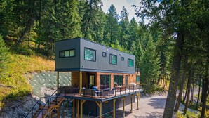 A modern two-story cabin with a deck, surrounded by forest. - NEW private hot tub & amazing lake views (Whitefish)