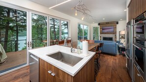 Een moderne keuken met een groot eiland, roestvrijstalen apparatuur en uitzicht op een bebost gebied.