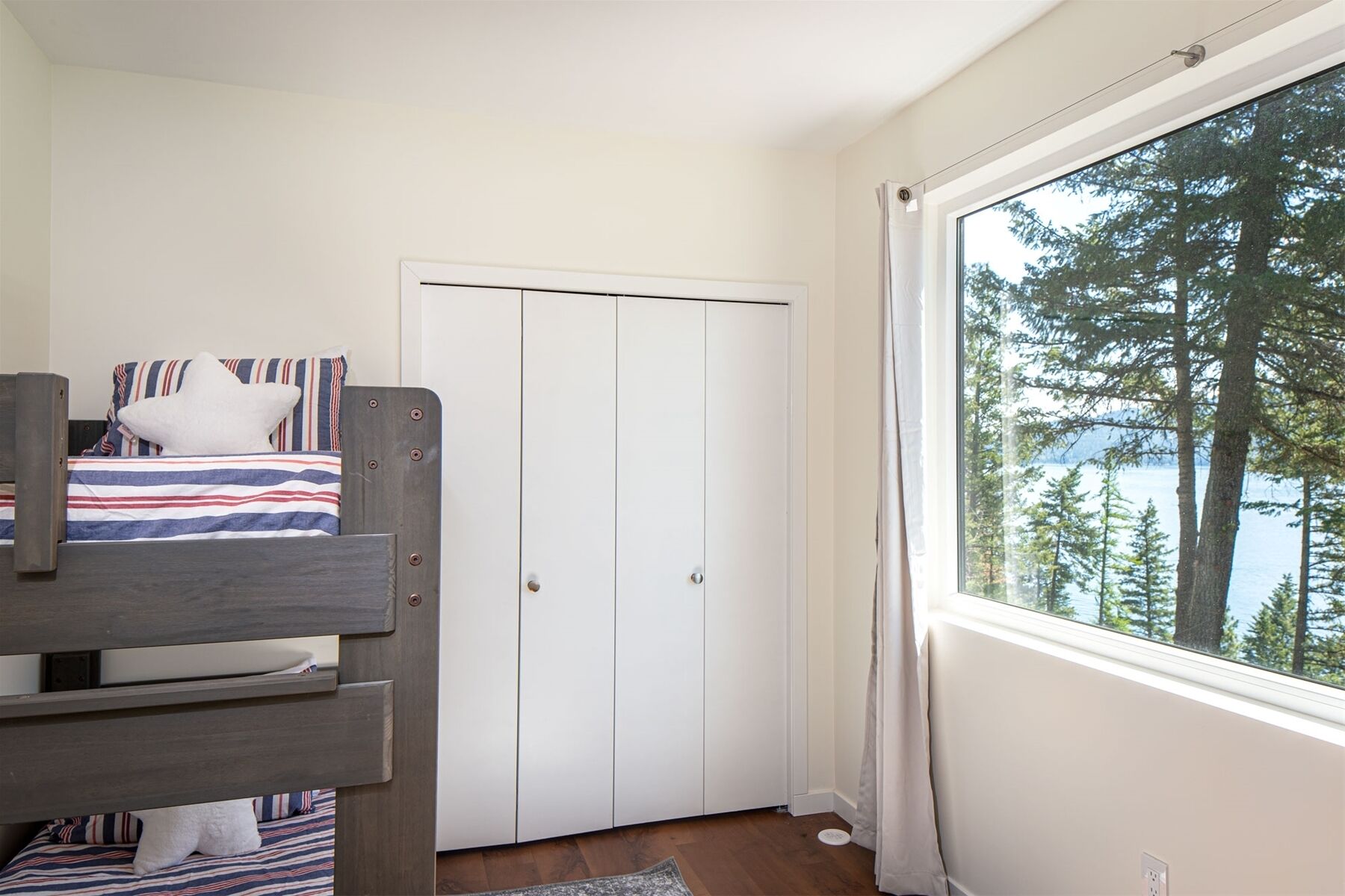 Une chambre avec un lit superposé, une armoire et une grande fenêtre donnant sur des arbres et l’eau.