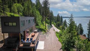 Une cabane moderne dotée d’une terrasse offrant une vue sur une zone boisée et un plan d’eau.