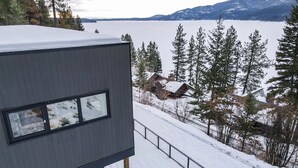 Een modern gebouw met een groot raam met uitzicht op een besneeerd landschap en een wateroppervlak.