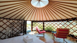 A yurt with a bed, a fan, a red chair, and a view of greenery. - Awaawa Yurts - Papa - Our Island (Waiheke Island)